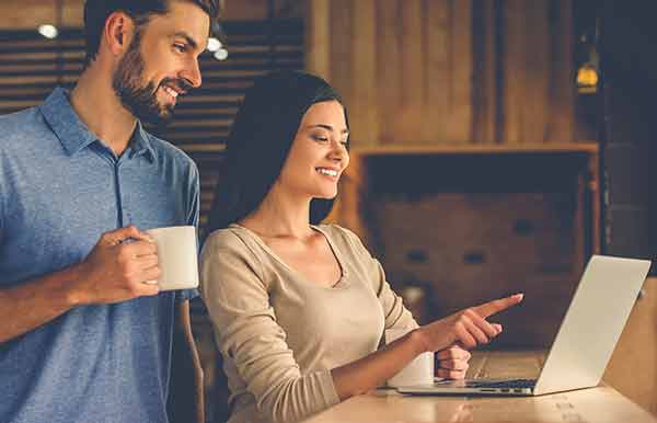A woman and man smiling while using a laptop and drinking coffee